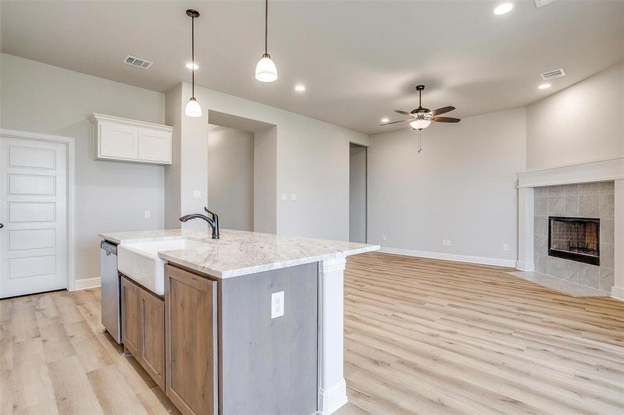 Kitchen with ceiling fan, white cabinets, light wood-type flooring, a tile fireplace, and a kitchen island with sink