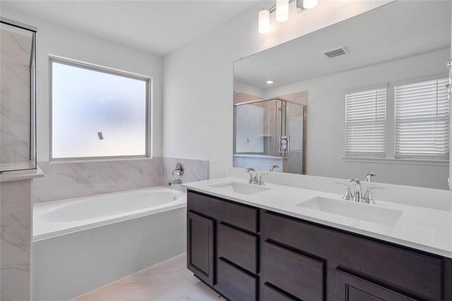 This primary bathroom is definitely move-in ready! Featuring an oversized tub and walk-in shower with tile surround, stained cabinets with light countertops, dual vanities, high ceilings, neutral paint, sleek and modern finishes.