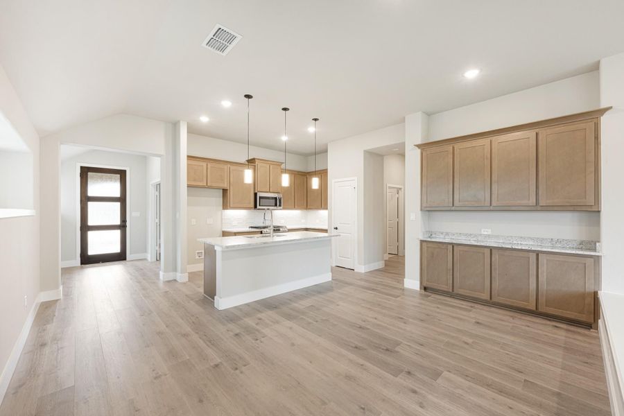 Open kitchen with light wood cabinets, center island, pendant lights, and light hardwood floors