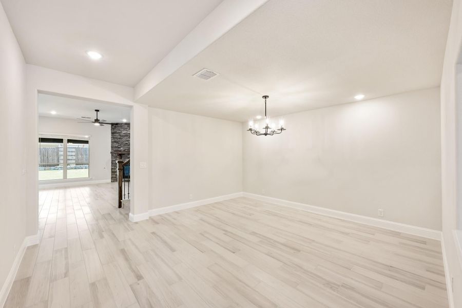 Open dining area with chandelier, light wood floors, and view into living room with stone fireplace Open dining area with chandelier, light wood floors, and view into living room with stone fireplace