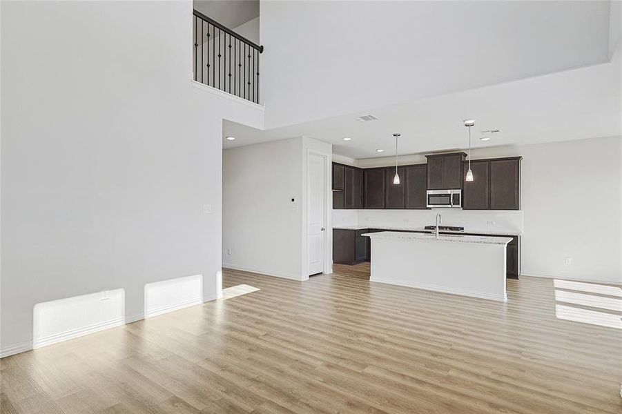 Kitchen featuring sink, light hardwood / wood-style floors, dark brown cabinetry, decorative light fixtures, and a center island with sink