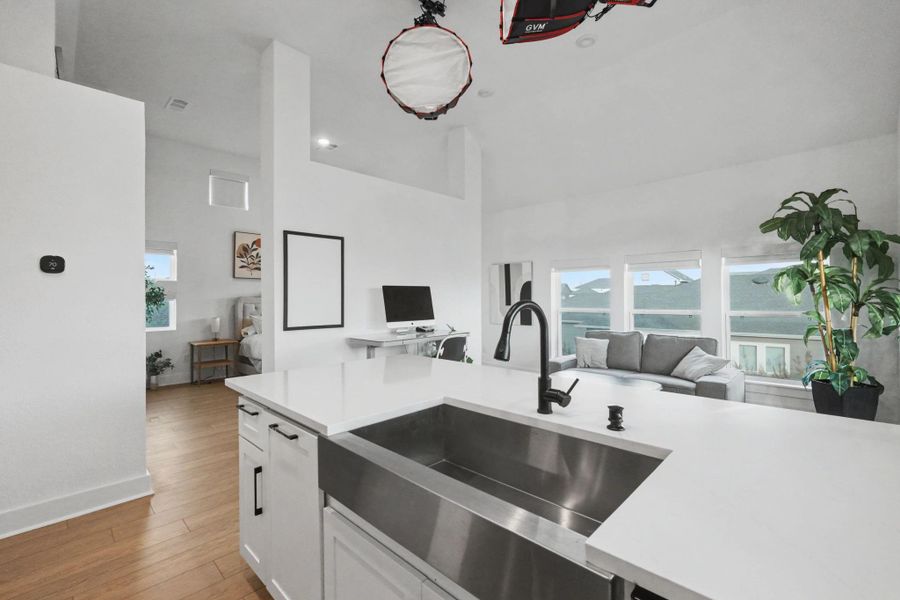 Open-concept garage apartment living area featuring soaring ceilings, expansive windows, and a sleek farmhouse sink with quartz counters. The bright layout seamlessly connects the kitchen, workspace, and living area for a modern, flexible lifestyle.