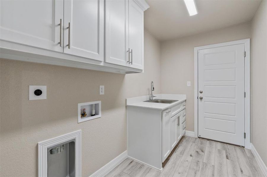 Laundry room featuring white cabinetry, a utility sink with a stone-finish countertop, light wood-finish flooring, and a modern paneled door Laundry room featuring white cabinetry, a utility sink with a stone-finish countertop, light wood-finish flooring, and a modern paneled door