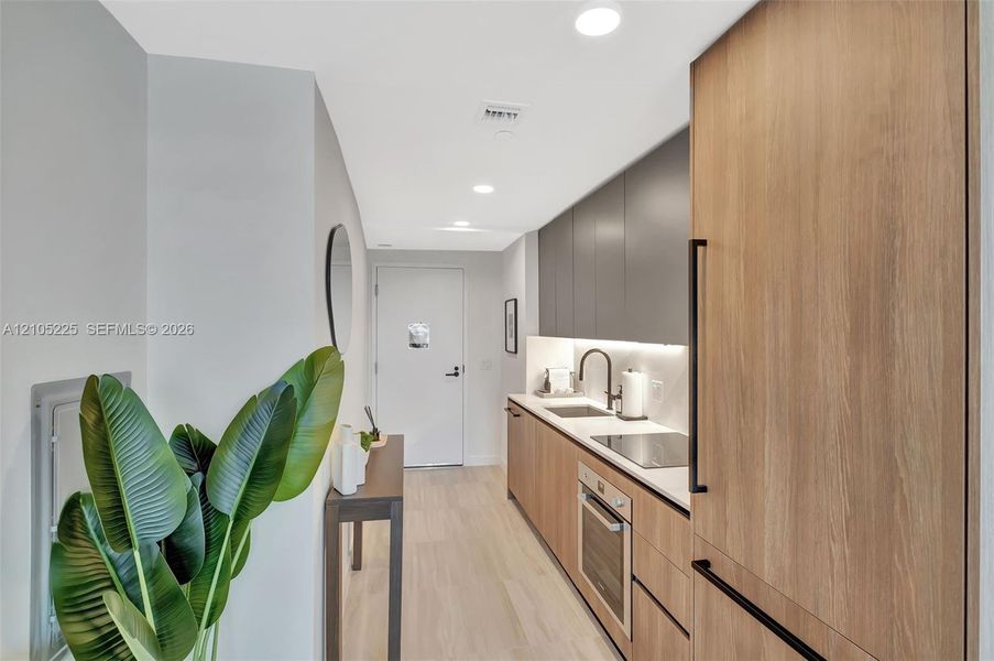 Integrated kitchen with wood-finish cabinetry, solid surface countertops, and stainless steel appliances