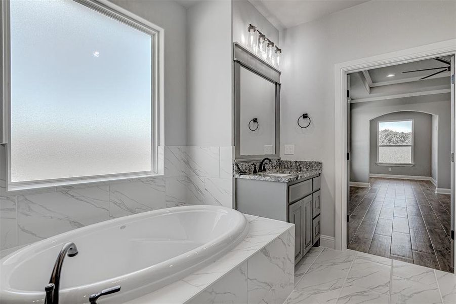 Bathroom with ceiling fan, tiled tub, and vanity