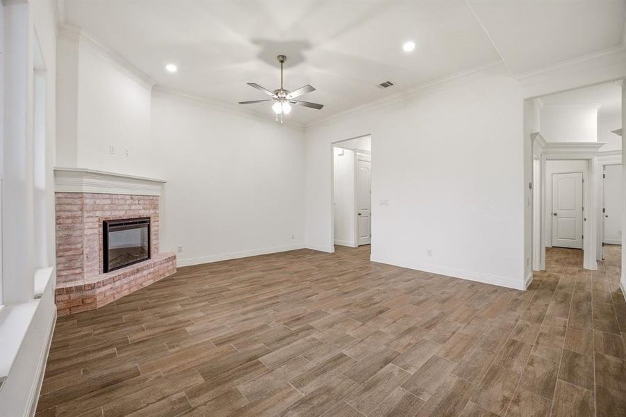 Living area featuring a brick fireplace, wood-look tile flooring, white walls, and a ceiling fan with integrated lighting