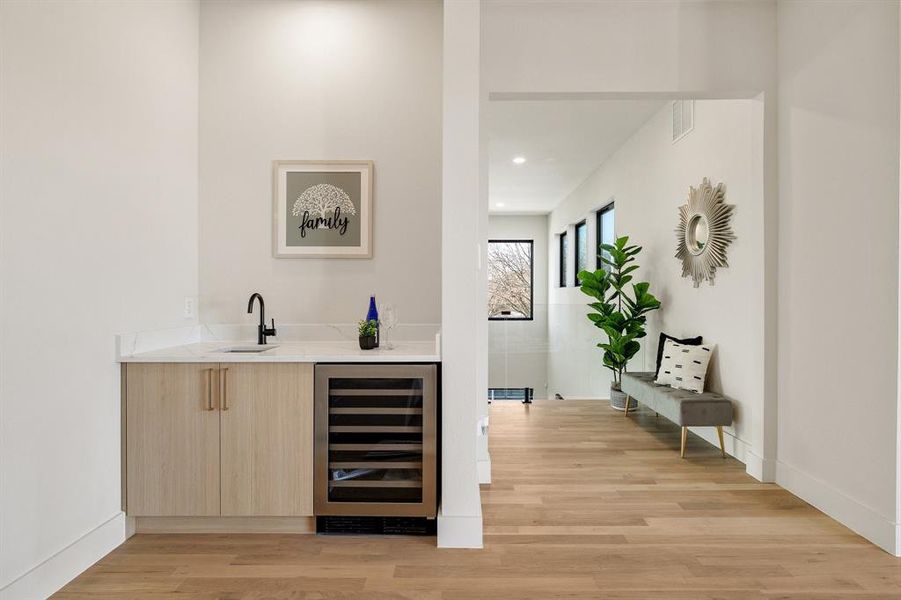 Bar with sink, light brown cabinets, light hardwood / wood-style flooring, and beverage cooler