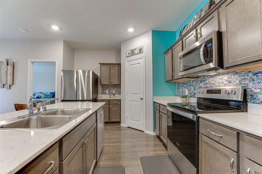 Kitchen with sink, dark hardwood / wood-style floors, decorative backsplash, light stone countertops, and appliances with stainless steel finishes