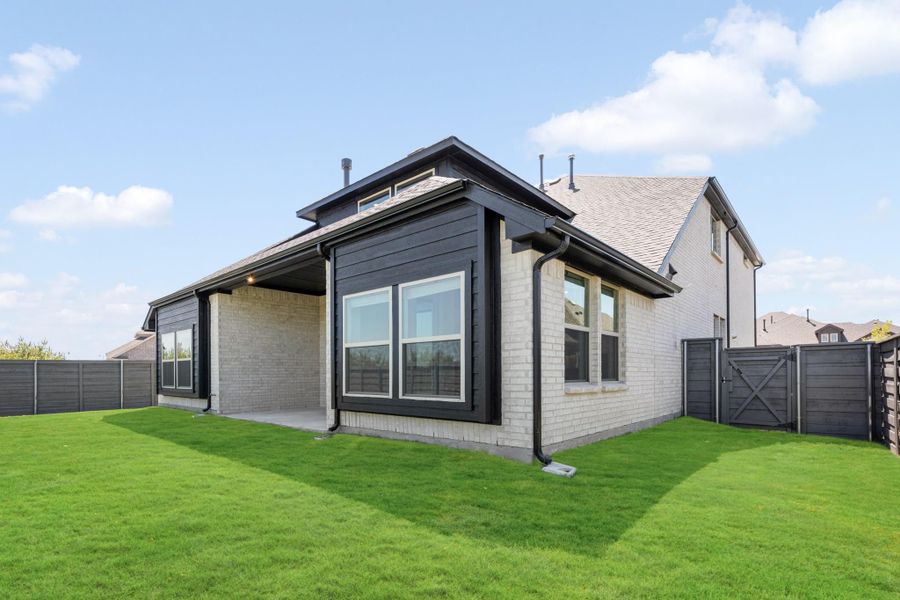 Home exterior rear view with dark siding, brick walls, covered patio, and fenced backyard with green lawn
