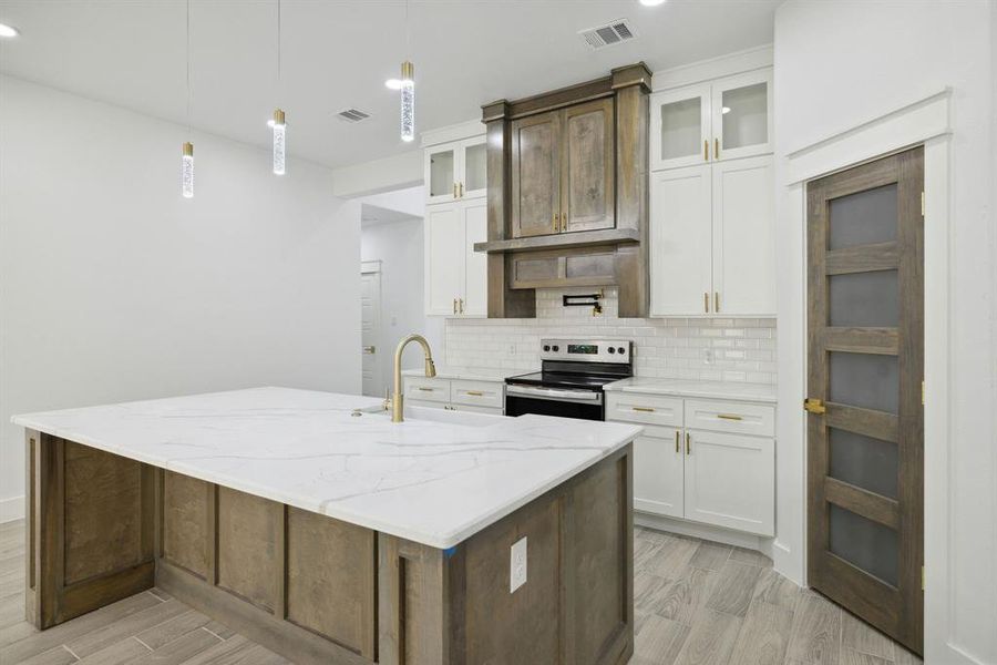 Kitchen with electric range, a kitchen island with sink, and white cabinetry