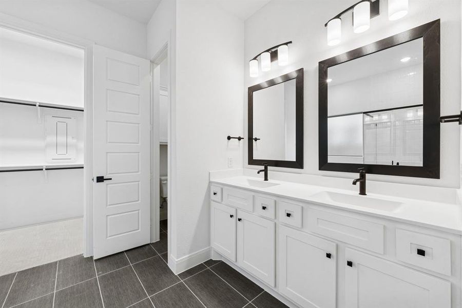 Bathroom with double vanity, a shower stall, a spacious closet, and dark tile patterned flooring Bathroom with double vanity, a shower stall, a spacious closet, and dark tile patterned flooring