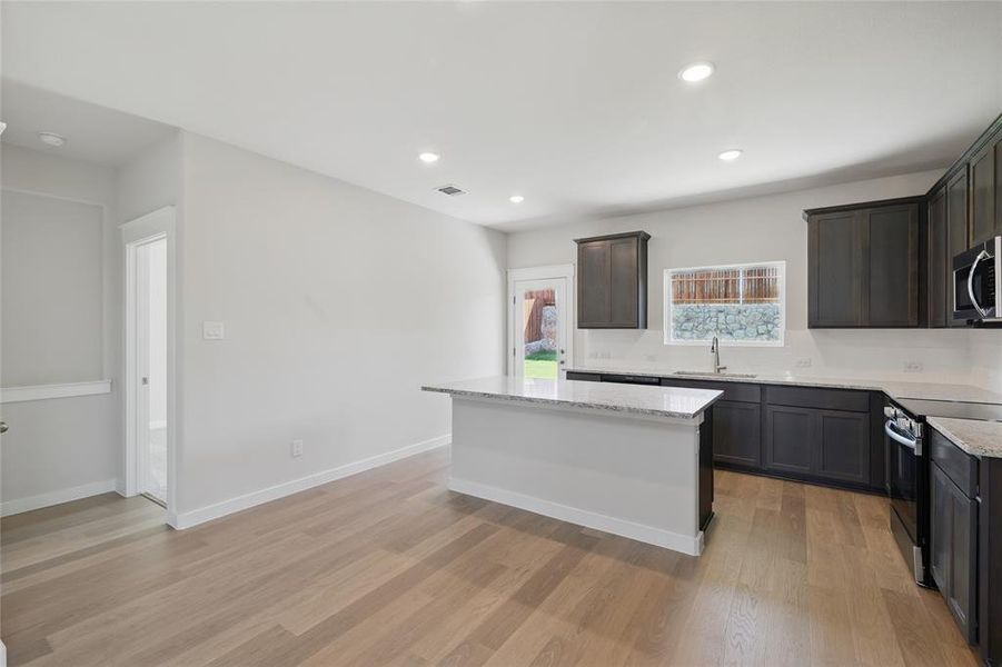 Kitchen with light stone counters, a kitchen island, stainless steel appliances, light wood-style floors, and recessed lighting