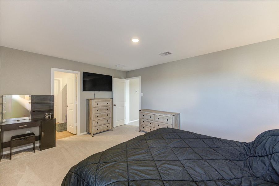 This bedroom features a cozy atmosphere with neutral walls, carpeted flooring, and ample natural light. It includes a dresser, a wall-mounted TV, and a vanity. There's an en suite bathroom and a spacious closet for convenience.