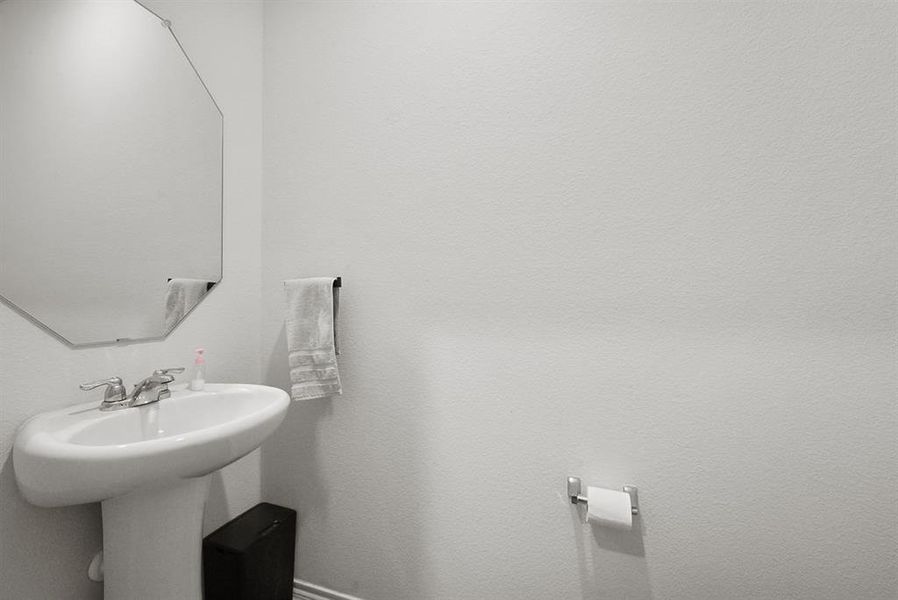 White pedestal sink with a chrome two-handle faucet, featuring an octagonal wall-mounted mirror