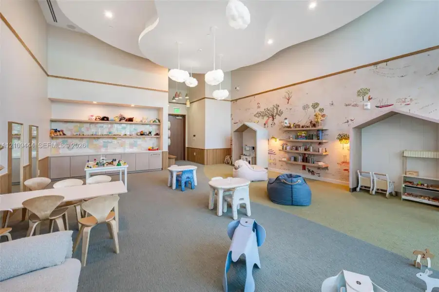 Expansive room featuring a decorative curved ceiling design, integrated cloud-style pendant lighting, built-in lower cabinetry with a horizontal shelving display, wall-mounted floating wood shelves, and house-shaped architectural alcoves