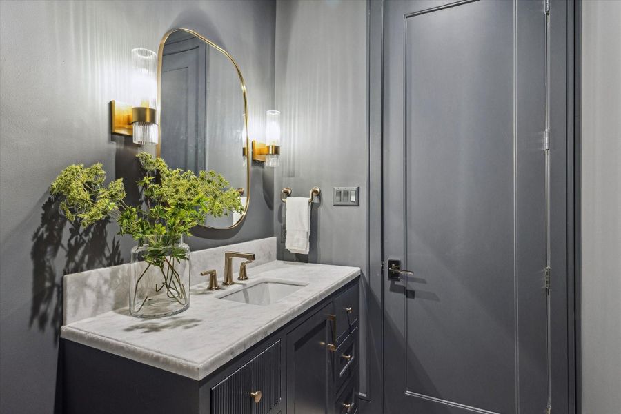 The second floor powder bath is decorated with marble countertops, gold finishes, and dark cabinetry. An upstairs powder room means guests in the media room don’t need to use one of the en-suites or go downstairs.