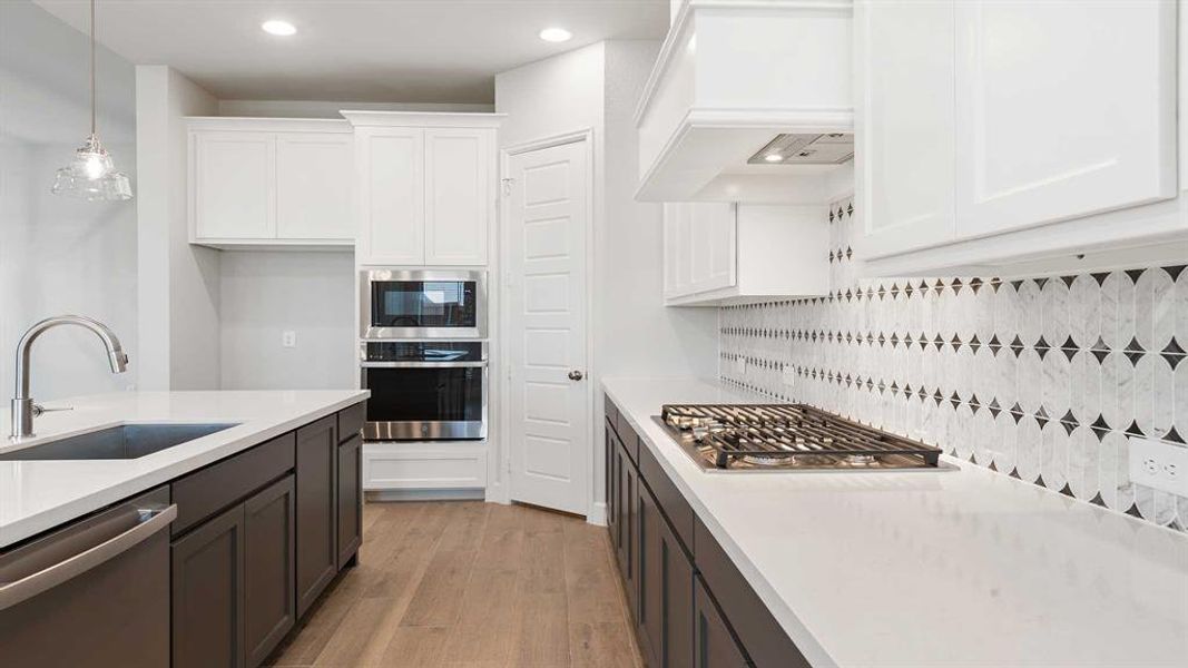 Kitchen featuring white cabinets, appliances with stainless steel finishes, tasteful backsplash, light hardwood / wood-style floors, and custom range hood