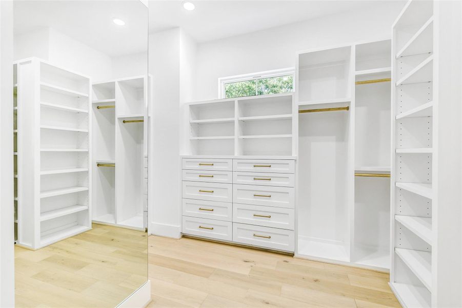 Step into a bespoke walk-in closet designed for both function and elegance. Featuring built-in shelving and drawers with soft-close shaker cabinetry, this space offers ample room forward robe organization. The brushed gold hardware, solid wood rods, and custom trim detailing reflect superior craftsmanship. A transom window brings in natural light, creating an airy and elevated dressing experience.