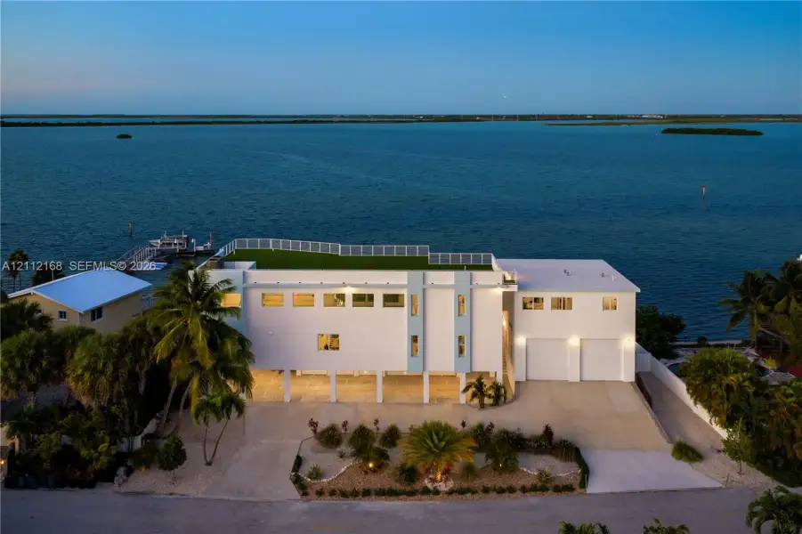 Waterfront estate featuring a rooftop terrace, elevated structural design, integrated two-car garage, private dock, and mature palm landscaping Waterfront estate featuring a rooftop terrace, elevated structural design, integrated two-car garage, private dock, and mature palm landscaping