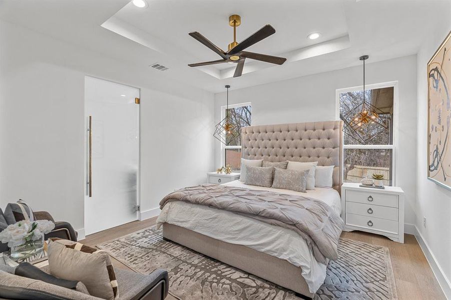 Bedroom with ceiling fan with notable chandelier, multiple windows, a tray ceiling, and light wood-type flooring