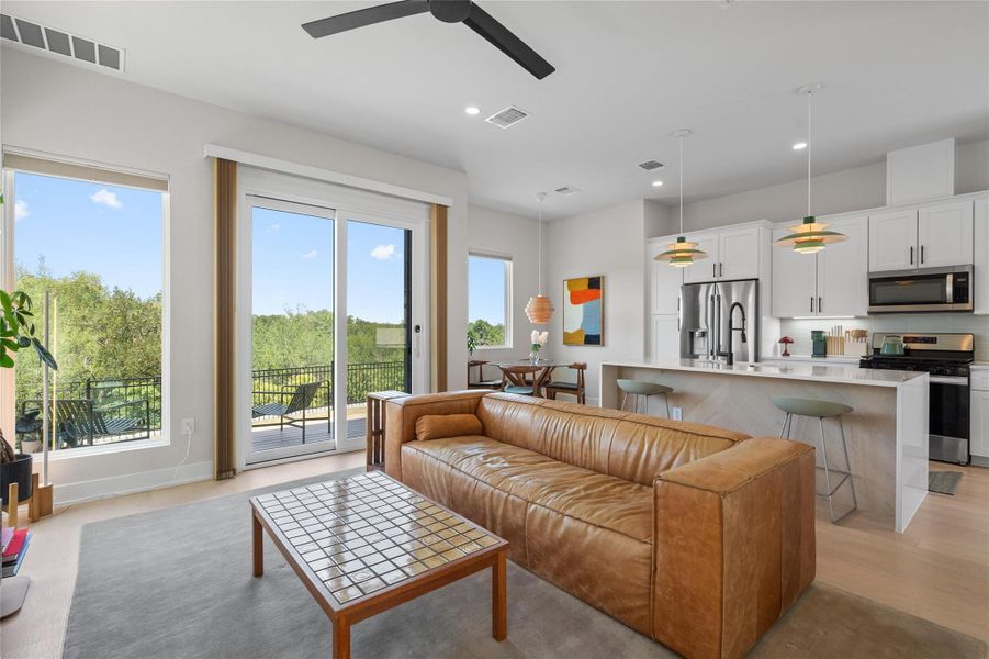 An open-concept living space with a gourmet kitchen flows seamlessly to an outdoor balcony with treetop views. An open-concept living space with a gourmet kitchen flows seamlessly to an outdoor balcony with treetop views.