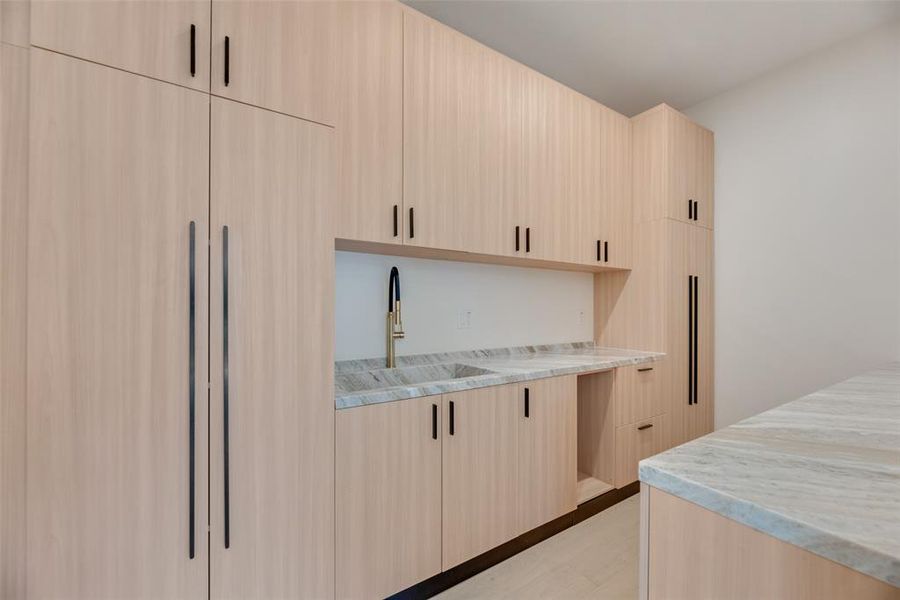 Kitchen featuring light brown cabinetry, light wood-type flooring, sink, and light stone countertops