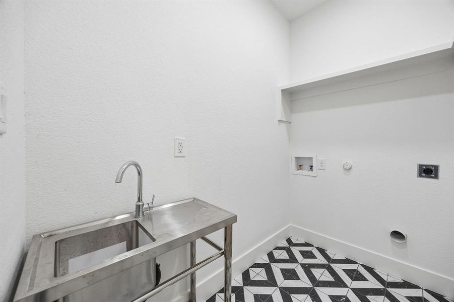 Utility room featuring a stainless steel sink with a chrome faucet, black and white geometric floor tiling, and a built-in shelf Utility room featuring a stainless steel sink with a chrome faucet, black and white geometric floor tiling, and a built-in shelf