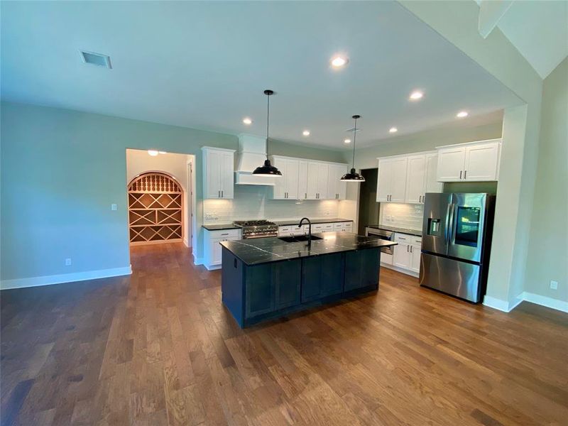 Kitchen with stainless steel appliances, dark hardwood / wood-style flooring, a center island with sink, and backsplash