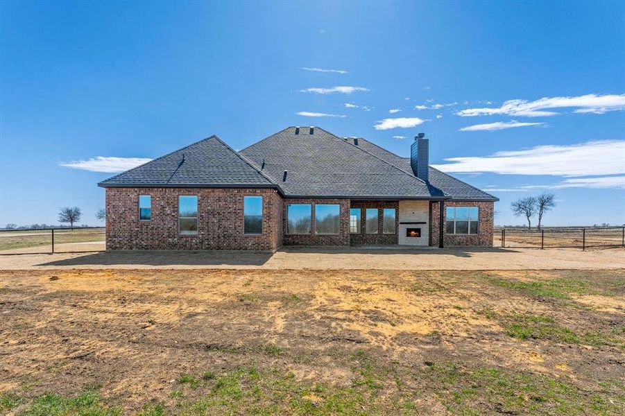 Rear view of property featuring a shingled roof, a patio area, brick siding, and fence