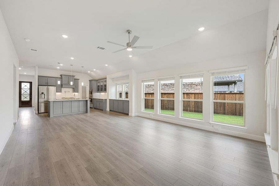 Open living area with hardwood floors and ceiling fan, flowing into kitchen with gray cabinets and island Open living area with hardwood floors and ceiling fan, flowing into kitchen with gray cabinets and island
