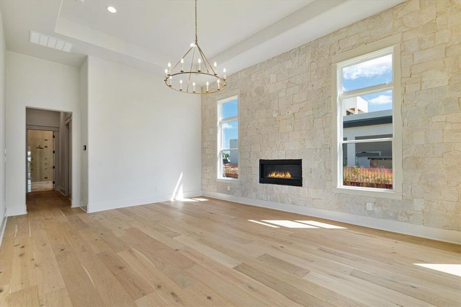 Unfurnished living room featuring light wood finished floors, a chandelier, a fireplace, a raised ceiling, and recessed lighting