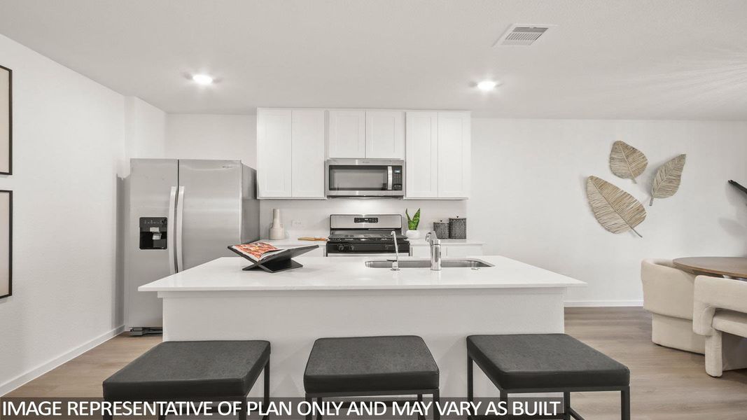 Kitchen featuring a kitchen bar, stainless steel appliances, a kitchen island with sink, light wood-style floors, and white cabinets