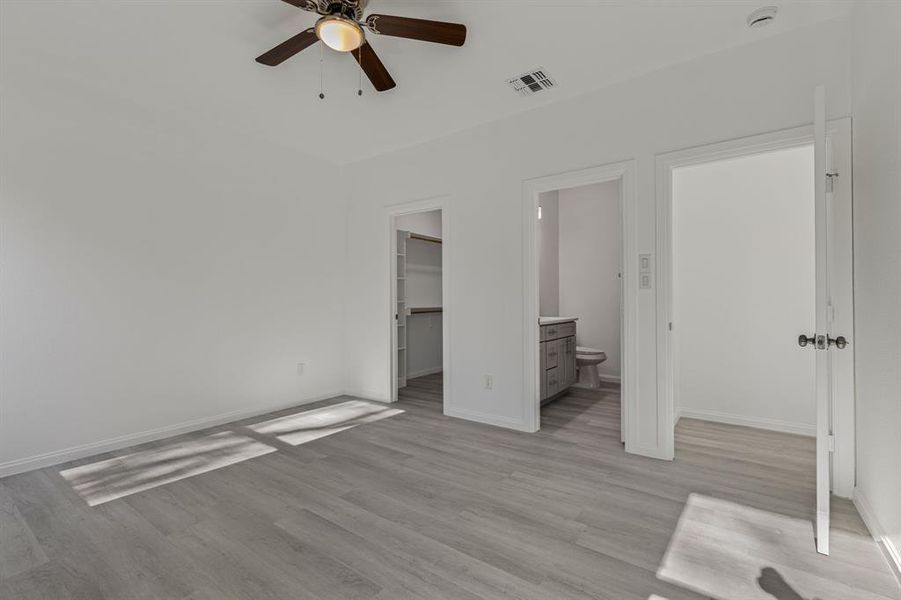 Unfurnished bedroom with light wood-style flooring, ensuite bathroom, a ceiling fan, and a walk in closet