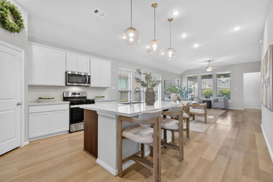 This spacious, open-concept kitchen and living area features modern white cabinetry, stainless steel appliances, and a large island with seating. The room is well-lit with stylish pendant lights and natural light from large windows, offering a welcoming and airy atmosphere. This spacious, open-concept kitchen and living area features modern white cabinetry, stainless steel appliances, and a large island with seating. The room is well-lit with stylish pendant lights and natural light from large windows, offering a welcoming and airy atmosphere.