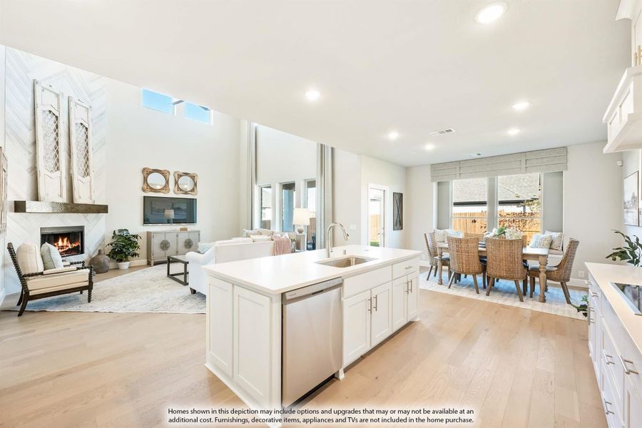 Open-concept kitchen with white island, flowing into dining area and living room with fireplace and hardwood floors