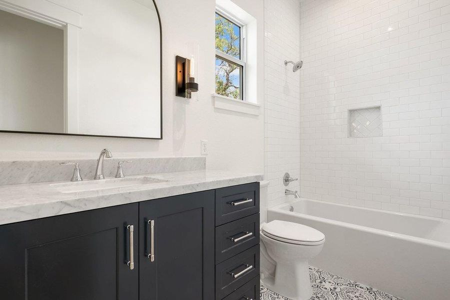 Bathroom featuring a dark vanity with a light-colored countertop, an undermount sink, a large mirror, and patterned floor tiles
