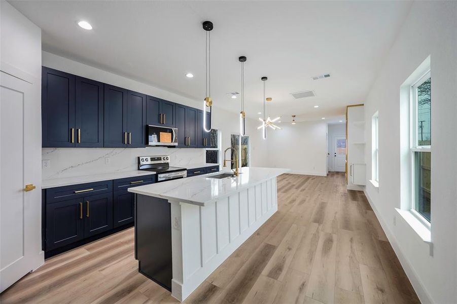 Kitchen featuring sink, appliances with stainless steel finishes, a kitchen island with sink, decorative backsplash, and decorative light fixtures