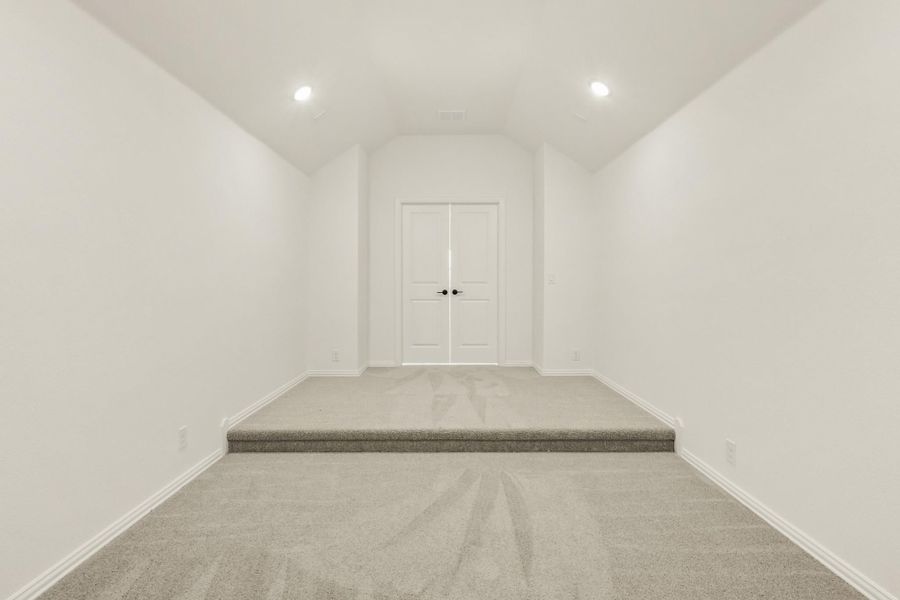 Empty room with gray carpet, vaulted ceiling, recessed lights, and raised platform area with double doors Empty room with gray carpet, vaulted ceiling, recessed lights, and raised platform area with double doors