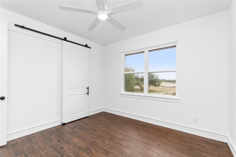 Unfurnished bedroom with a barn door, dark wood finished floors, baseboards, and a ceiling fan Unfurnished bedroom with a barn door, dark wood finished floors, baseboards, and a ceiling fan