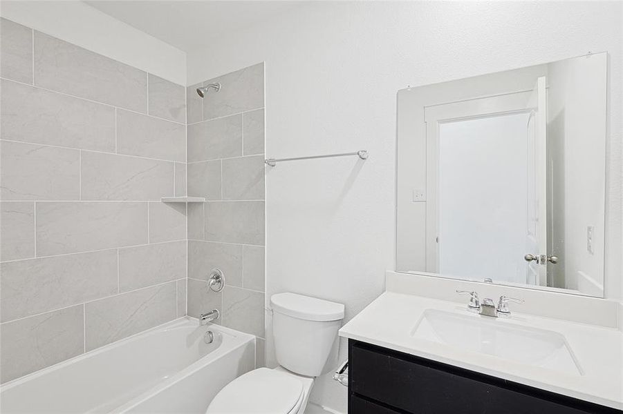 Full bathroom with vanity, tiled shower / bath combo, and toilet