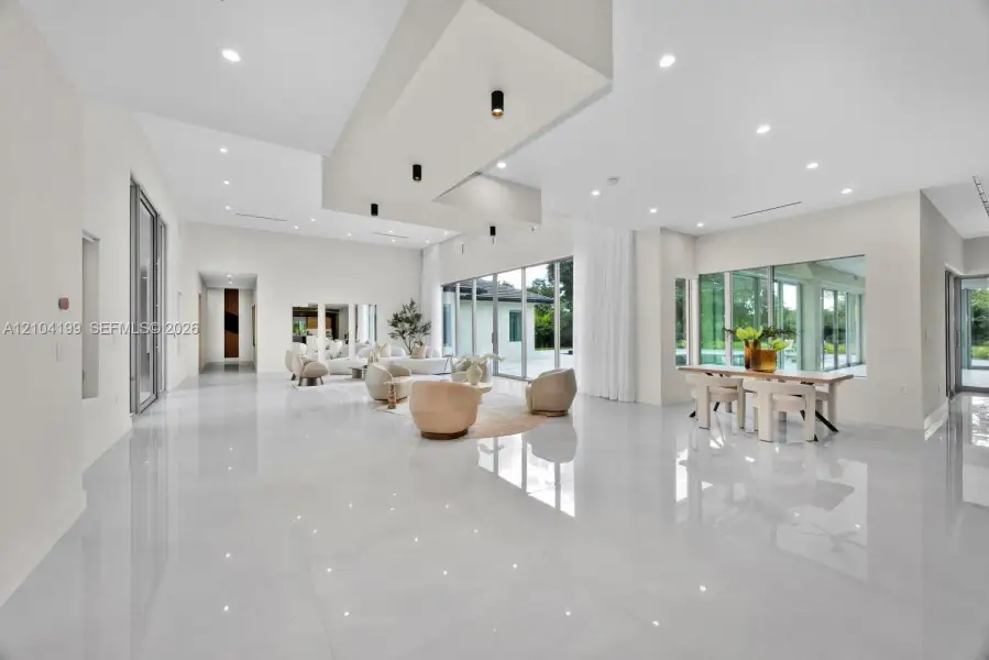 Open-concept living space featuring high-gloss tile flooring, recessed lighting, a tiered tray ceiling with cylindrical pendant fixtures, and floor-to-ceiling glass panel walls