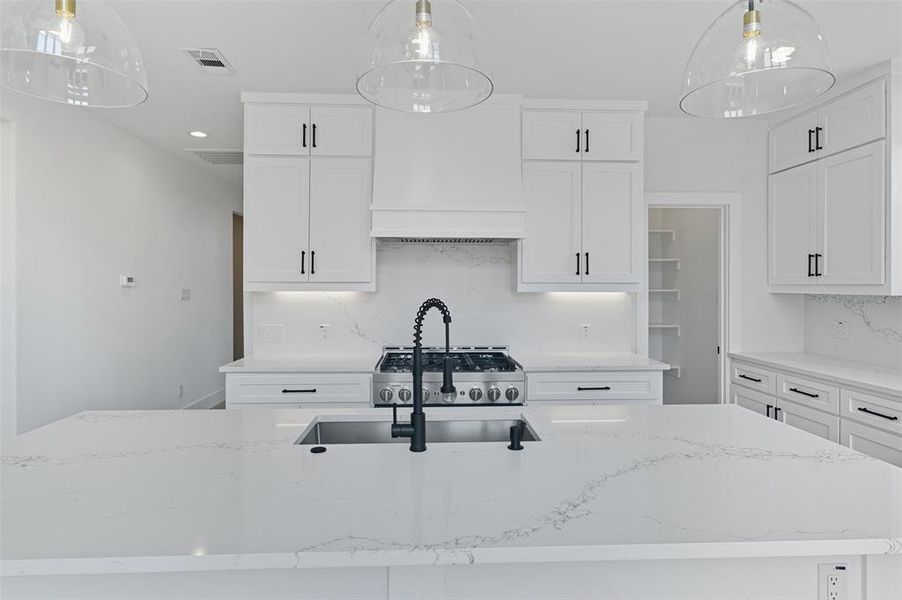 Kitchen featuring decorative light fixtures, decorative backsplash, light stone counters, white cabinets, and a center island with sink