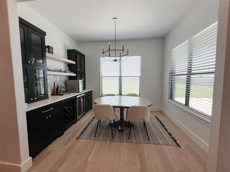 Dining room featuring a chandelier, light wood-type flooring, beverage cooler, and a dry bar