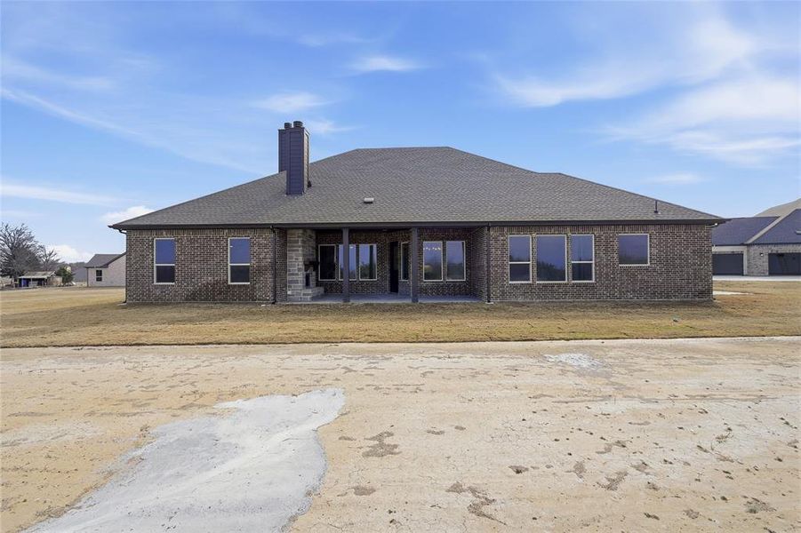 Back of house featuring a patio area, a chimney, brick siding, and a lawn