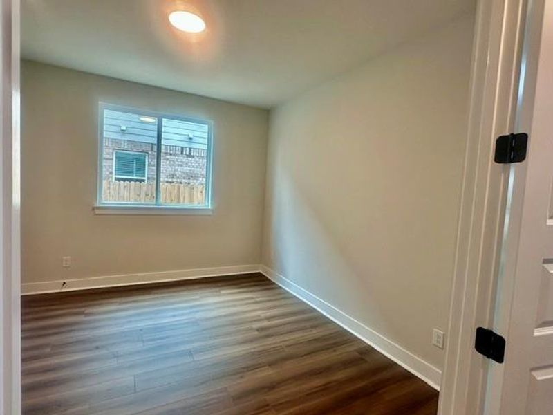 A quiet bedroom featuring resilient wood-look flooring and a naturally illuminated window. A quiet bedroom featuring resilient wood-look flooring and a naturally illuminated window.