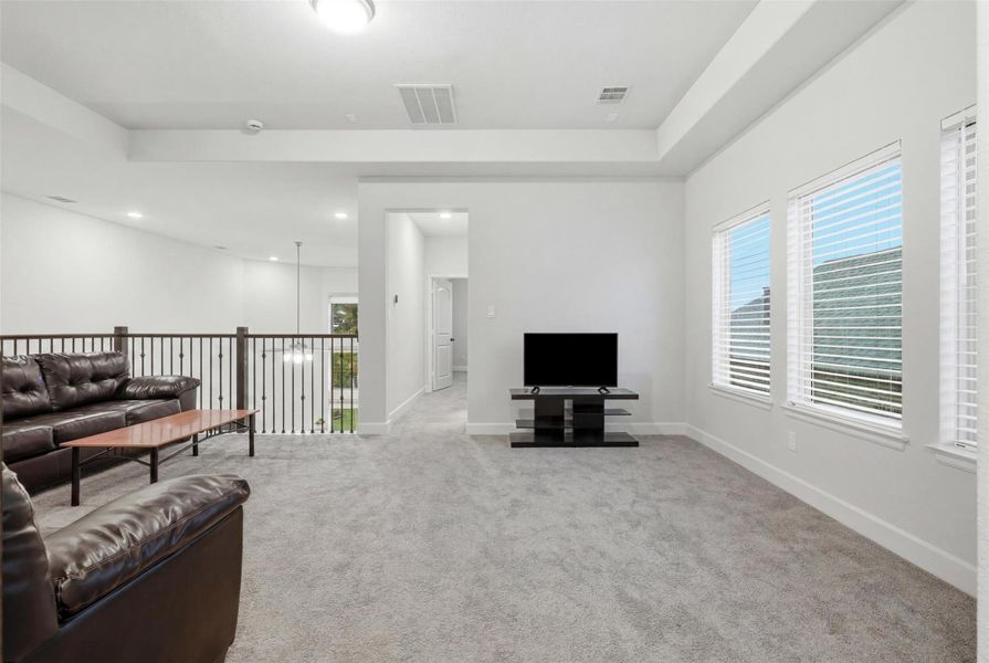 Spacious, bright living area with plush carpet, large windows, and modern lighting. Includes a cozy seating arrangement, TV setup, and open railing overlooking the lower level. Perfect for relaxation and entertaining. Spacious, bright living area with plush carpet, large windows, and modern lighting. Includes a cozy seating arrangement, TV setup, and open railing overlooking the lower level. Perfect for relaxation and entertaining.