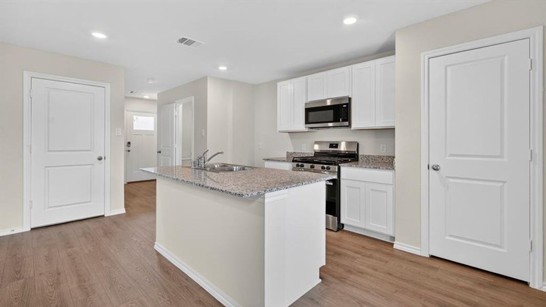 Kitchen featuring white cabinetry, stainless steel appliances, a center island with a double basin sink, granite countertops, and wood-finish flooring