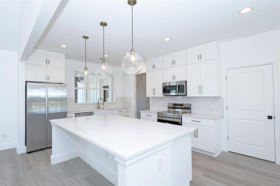 Kitchen with appliances with stainless steel finishes, light wood-type flooring, a kitchen island, decorative backsplash, and recessed lighting