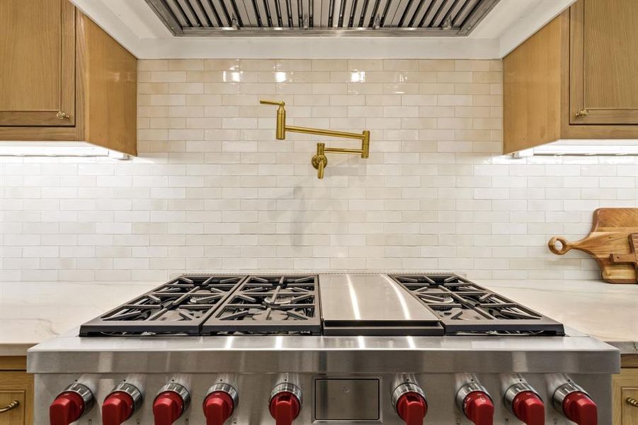 Stainless steel gas range with a griddle feature, set against a cream subway tile backsplash with a gold-finish pot filler