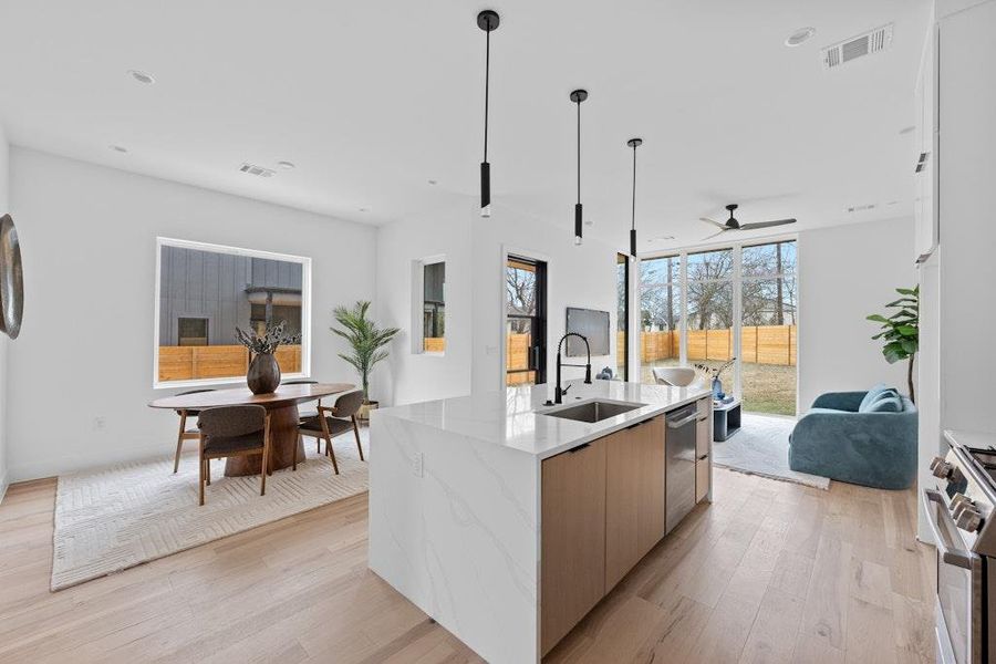 Kitchen featuring light wood-style floors, light stone countertops, pendant lighting, and appliances with stainless steel finishes